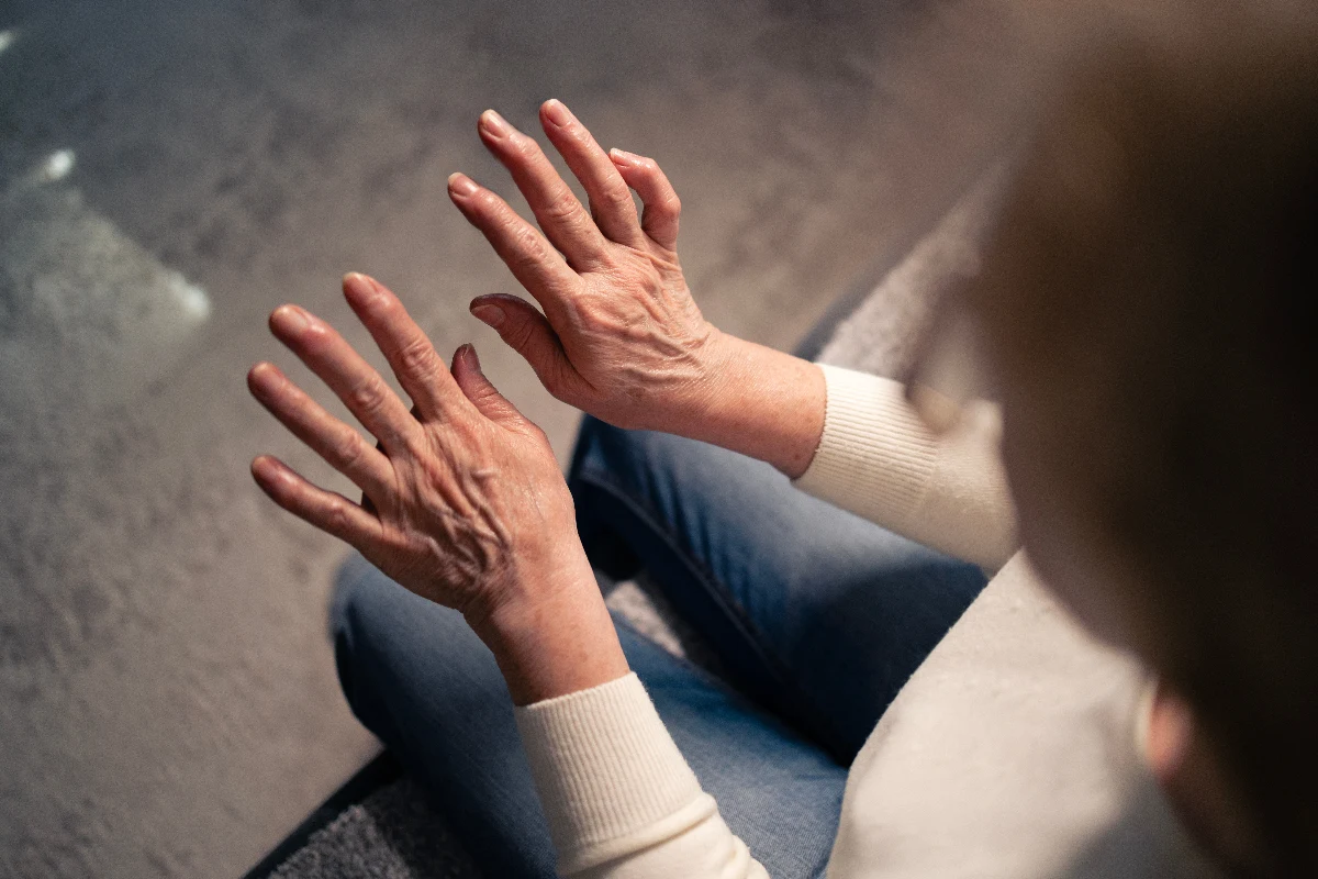 Elderly person viewing hands under gentle light, showing wrinkled skin and outstretched fingers. Relaxed, contemplative mood with casual sweater and jeans.