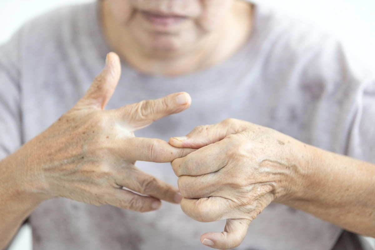 Elderly person in a gray shirt massaging their arthritic fingers, conveying a sense of discomfort and care. Hands are the focus against a blurred background. Boutonnière Deformity Surgeon Dr. Rod French Vancouver