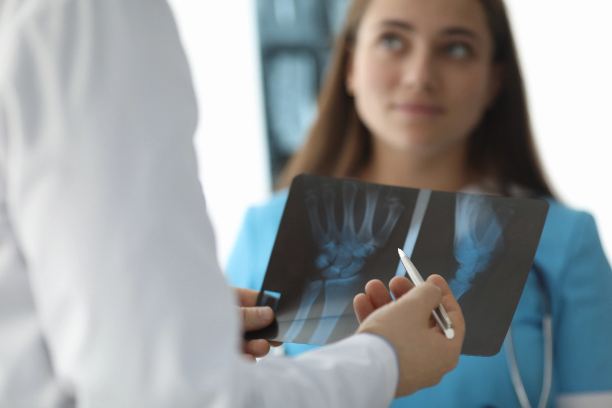 A doctor holds and points to a wrist X-ray while discussing it with a patient dressed in blue scrubs. The mood appears professional and attentive. Scaphoid Fracture & Nonunion Surgeon Dr. French Vancouver