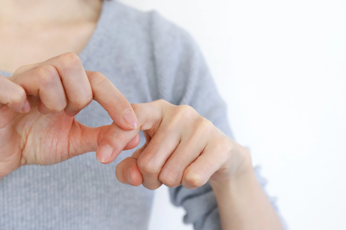 Close-up of hands in gentle motion; a person in a gray sweater presses one finger against another in a soothing, self-care gesture against a neutral background. Trigger Finger Release Surgery in Vancouver Dr. Rod French